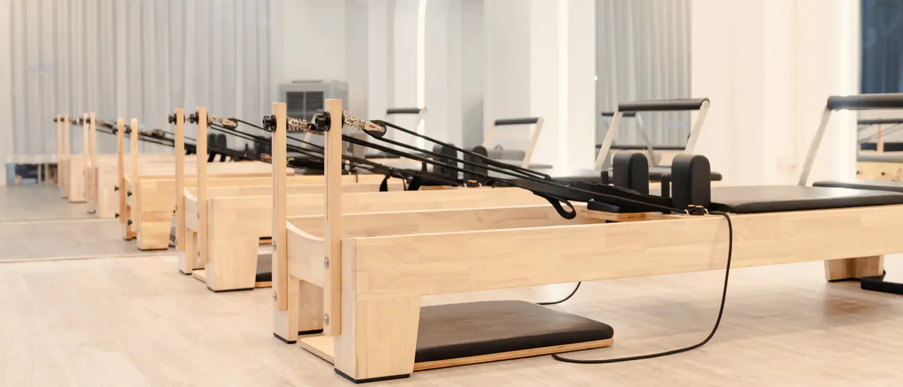 Sala de un estudio de Pilates con una fila de reformers de madera clara y cortinas de lino al fondo