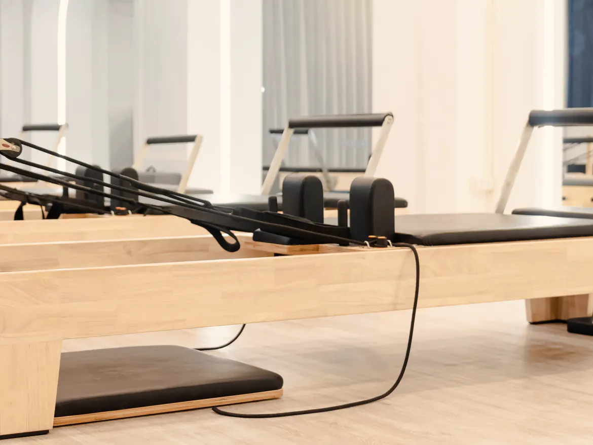 Sala de un estudio de Pilates con una fila de reformers de madera clara y cortinas de lino al fondo